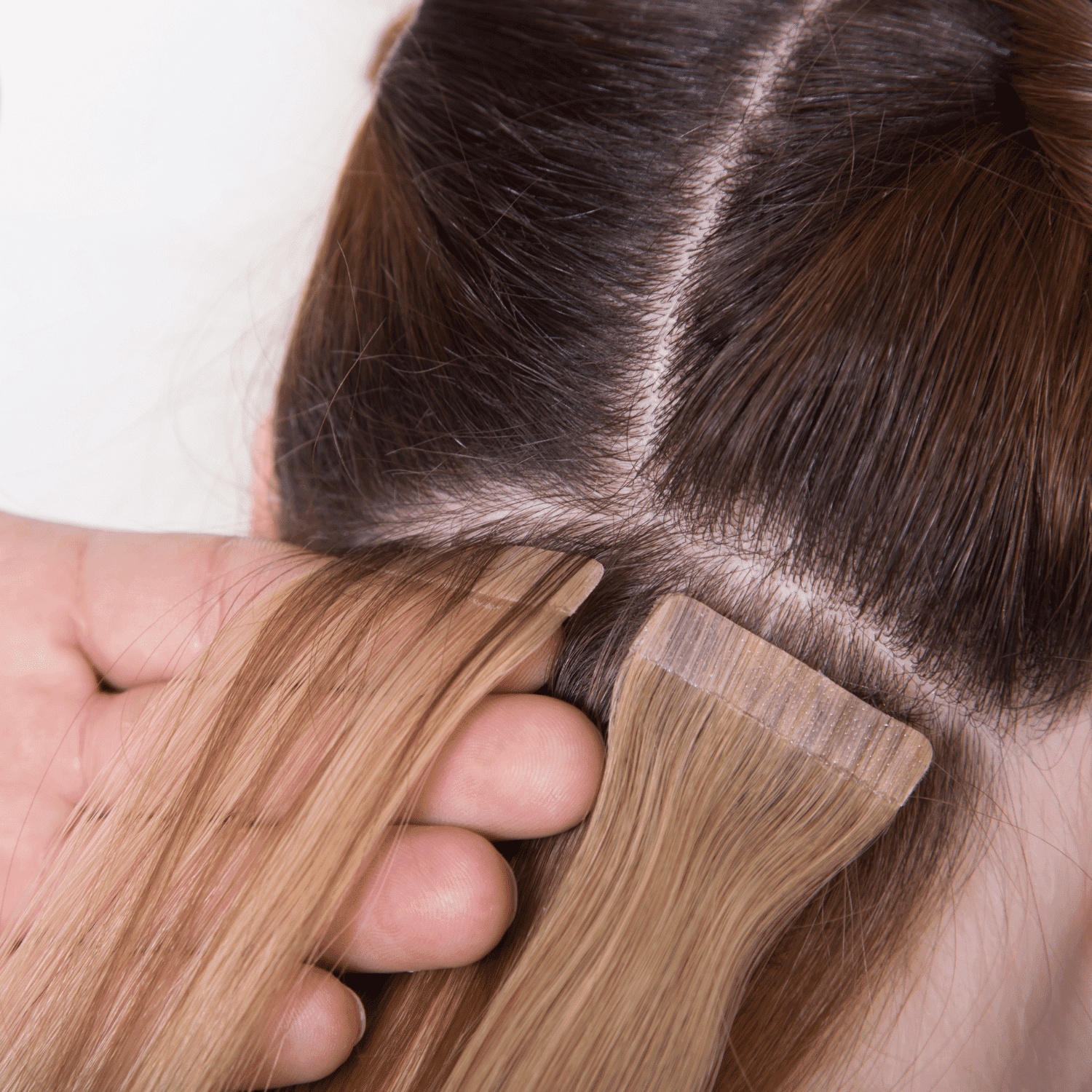 Hair extensions being applied to brown hair with adhesive tape.